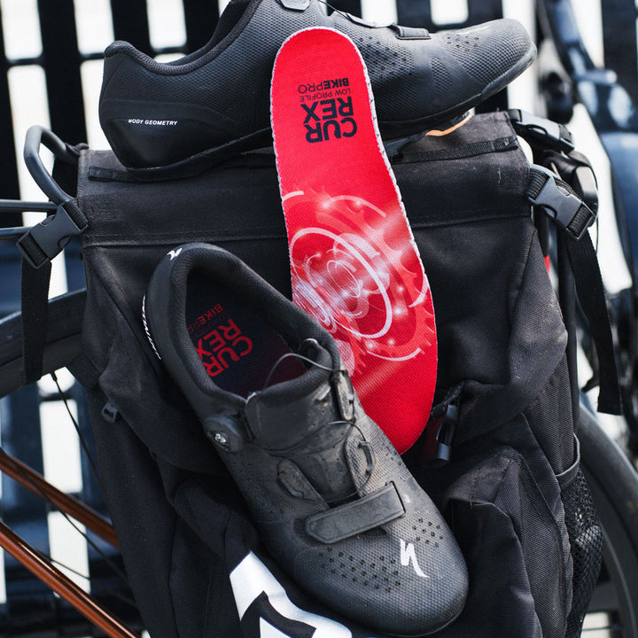 Black cycling shoes sitting against backpack with CURREX BIKEPRO red low profile insoles #1-wahle-dein-profil_low