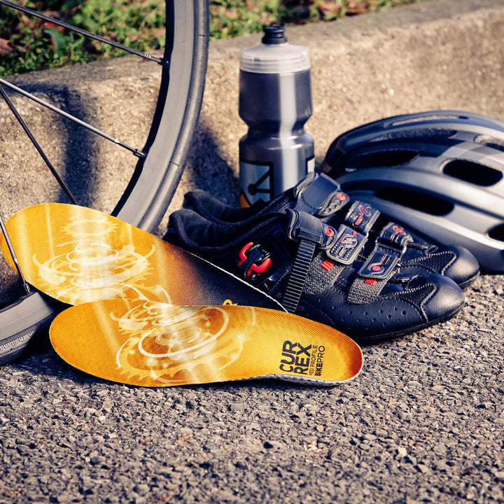 CURREX BIKEPRO yellow medium profile insoles sitting against bicycle wheel, cycling shoes, helmet, and water bottle #1-wahle-dein-profil_med