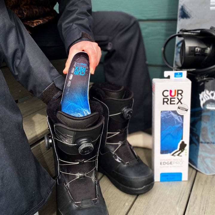 Person sitting on bench preparing to go skiing by placing CURREX EDGEPRO blue high profile insoles into black ski boots #1-wahle-dein-profil_high