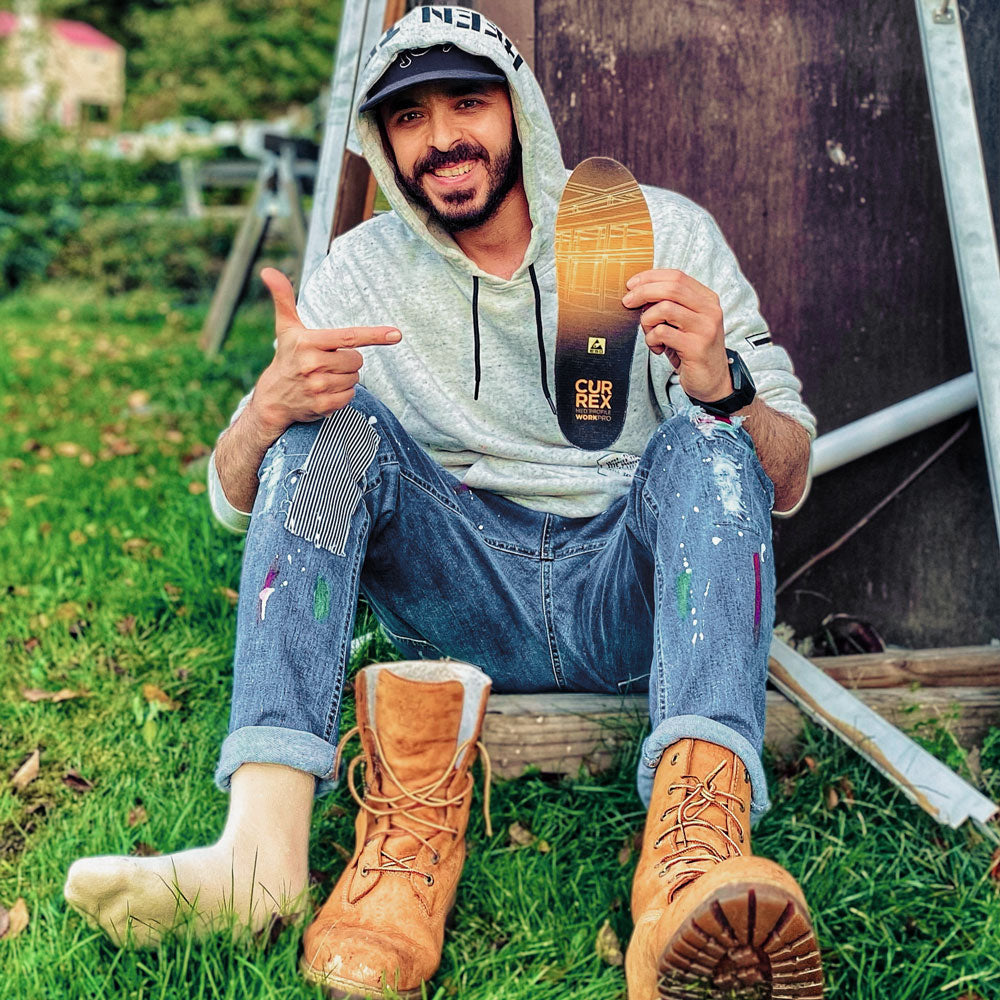 Man sitting in yard holding up a pair of CURREX WORK yellow medium profile insoles for his work boots #1-wahle-dein-profil_med